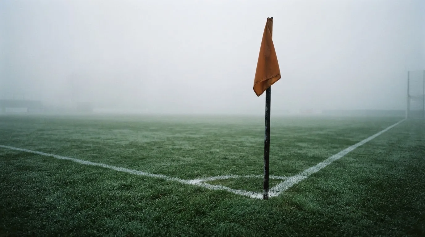 Der Rand eines Spielfelds mit weißer Linie und Eckfahne bei Nebel am frühen Morgen, ohne Menschen.