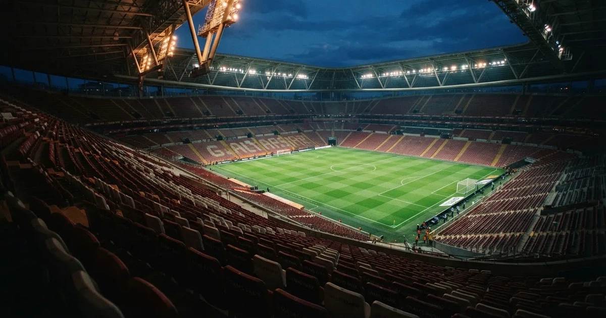 Leere Sitzreihen eines großen Stadions unter Flutlicht, dahinter die ferne Sicht auf den hell beleuchteten Rasen nach Sonnenuntergang.