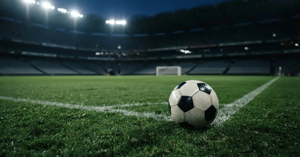 Ein Fußball liegt auf dem Rasen eines leeren Stadions bei Flutlicht, im Hintergrund unscharfe Tribünen ohne erkennbare Beschriftung.