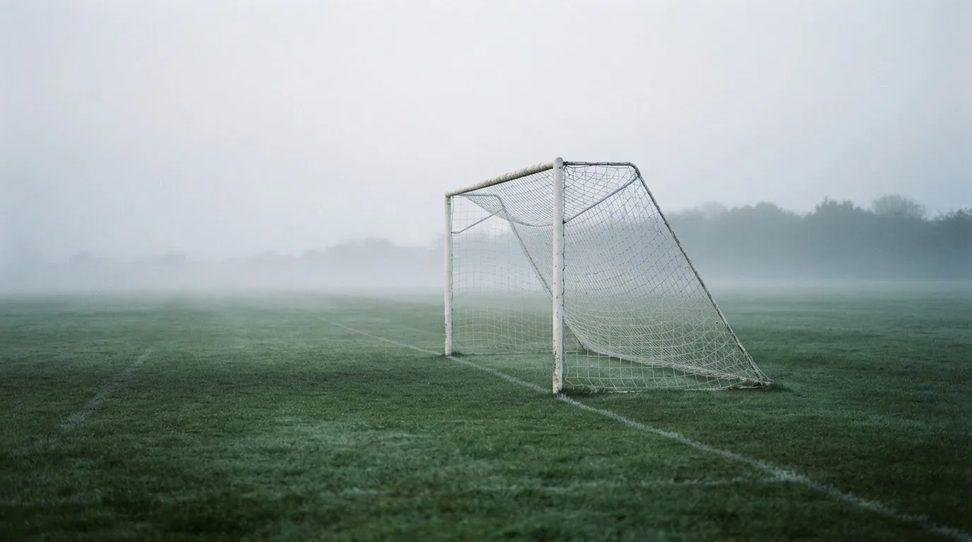 Ein Fußballtor mit Netz im Morgennebel auf einem leeren Platz, die Linien nur schwach zu erkennen.
