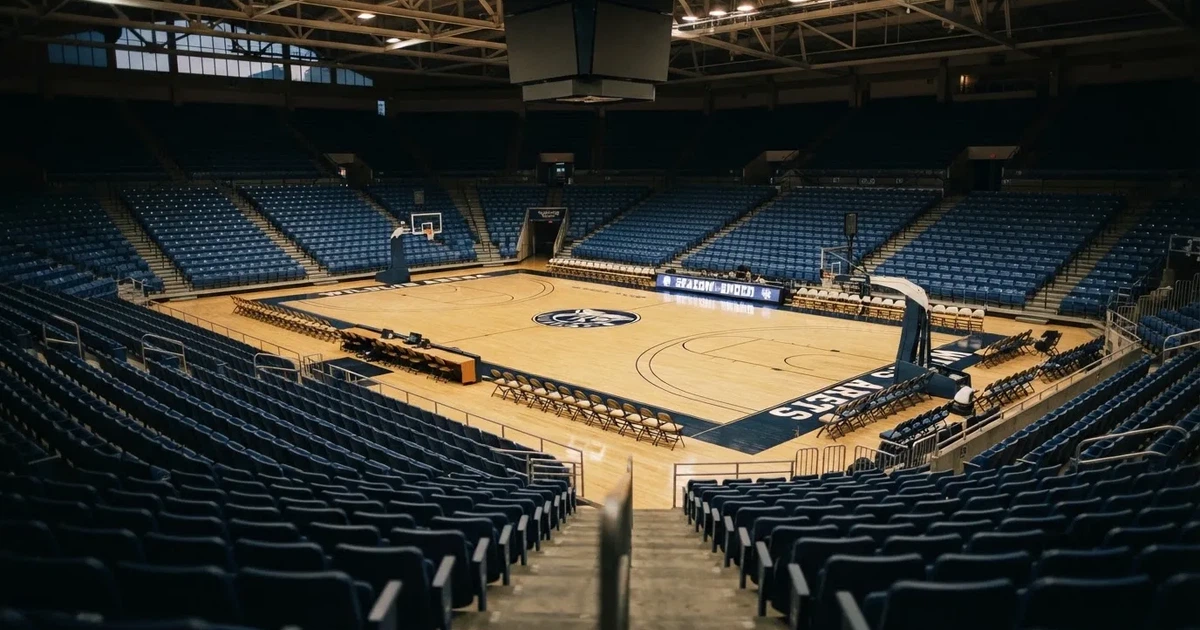 Eine leere Basketballhalle von einer oberen Tribünenreihe aus gesehen, Parkett und Körbe im Licht der Hallenstrahler.