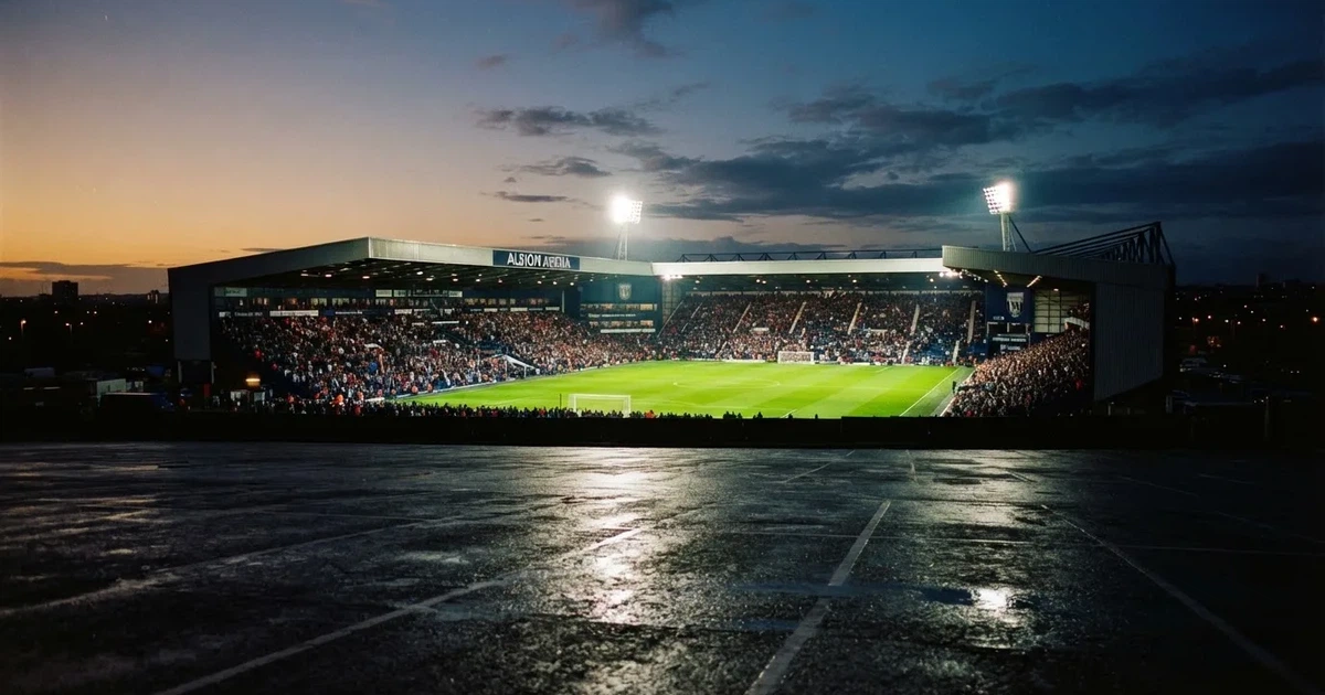 Ein Fußballstadion unter Flutlicht aus großer Entfernung, davor ein dunkler Parkplatz und ein heller Abendhimmel.