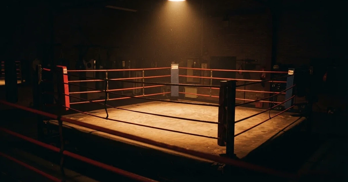 Ein Boxring mit gespannten Seilen in einer leeren Halle, ein einzelner Scheinwerfer leuchtet von oben auf die Ringmatte.