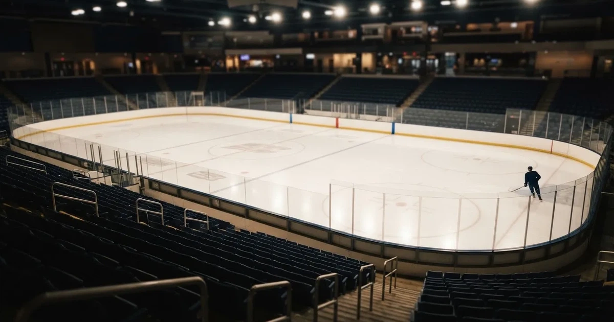 Eine Eishockeyhalle von der Tribüne aus gesehen, spiegelglatte Eisfläche, Banden ohne Schriftzüge, helles Flutlicht.