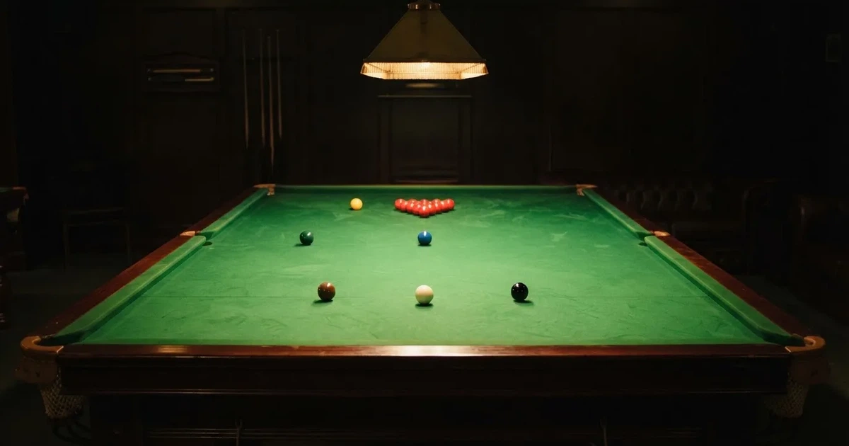 Ein Snookertisch mit grünem Tuch und aufgebauten roten Kugeln in einem abgedunkelten Raum unter einer hängenden Lampe.
