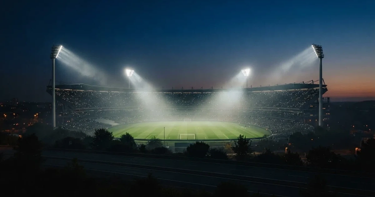 Ein leeres Stadion unter Flutlicht aus großer Entfernung gesehen, Dunst liegt über dem Rasen, die Tribünen sind nur als Lichtpunkte erkennbar.
