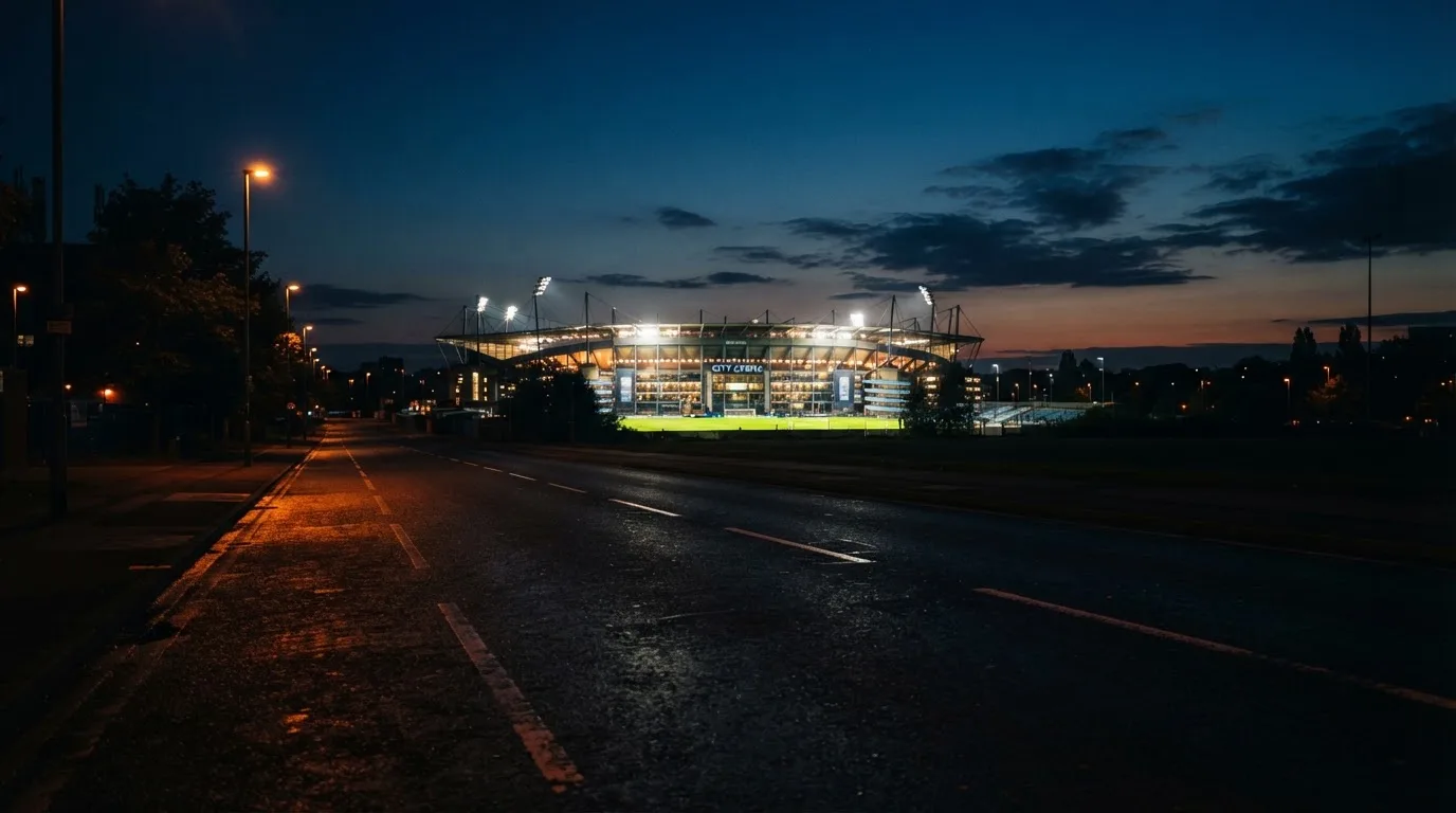 Ein Stadion unter Flutlicht aus großer Entfernung, davor eine leere Straße in der Abenddämmerung.